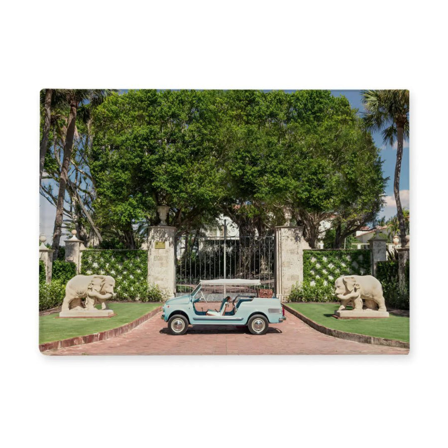 Vintage car parked in front of a gated entrance with stone elephants on either side.