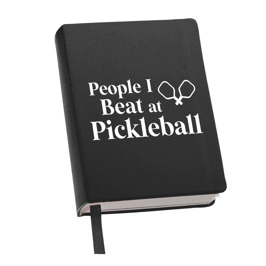 Black notebook with 'People I Beat at Pickleball' text and pickleball paddle icon on a white background
